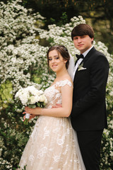 Handsome groom hug his bride in their wedding day. Background of flowering trees