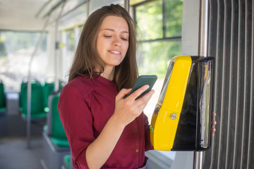 Female Woman paying conctactless with smartphone for the public transport in the tram. Yellow ticket machine in the modern tram