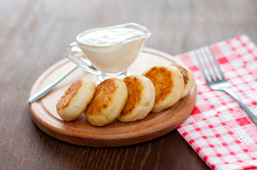Cheese pancakes with sour cream on a wooden board, with a fork and napkin horizontal format.