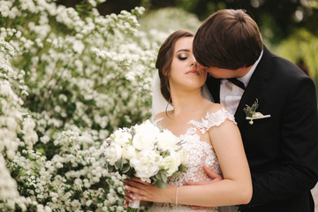 Handsome groom hug his bride in their wedding day. Background of flowering trees