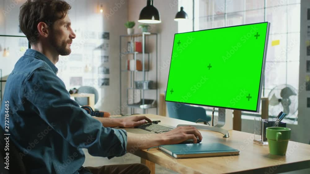 Poster young professional creative employee sits down and works on his personal computer with big green scr