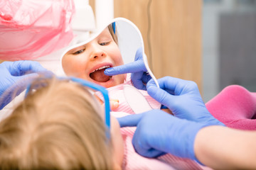 Obraz na płótnie Canvas Little girl looking at cured teeth thru the mirror in pediatric dental clinic