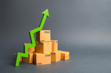 A pile of cardboard boxes and a green up arrow. The growth rate of production of goods and...