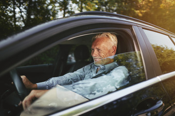 Senior man smiling while driving on a country road