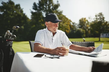 Gordijnen Smiling senior man relaxing after playing a round of golf © Flamingo Images