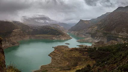 Papier peint photo  A reservoir in winter in the wild rugged mountains of the Spanish Sierra Nevada near the city of Granada. The clouds are floating low.  © wewi-creative