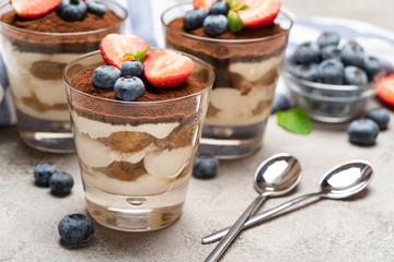 Classic tiramisu dessert with blueberries and strawberries in a glass on concrete background