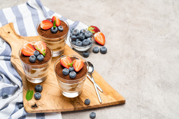 Classic tiramisu dessert with blueberries and strawberries in a glass on concrete background