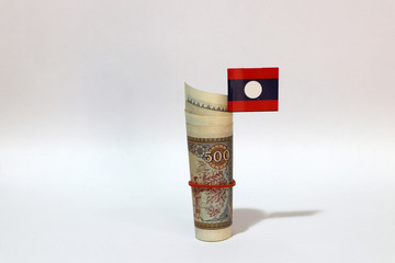 Rolled banknote money five hundreds Lao Kip and stick with mini Laos flag on white background.