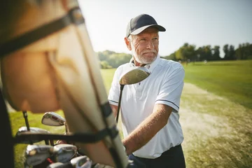 Selbstklebende Fototapeten Senior man preparing to play golf on a sunny day © Flamingo Images