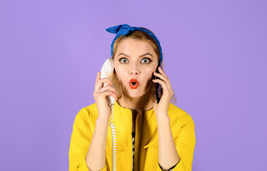 Stylish girl holds wired phone&cell phone. Surprised woman in headband holds handset&smartphone. Phones of different generations. Pinup girl with retro telephone&mobile phone. Technological evolution.