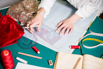 Obraz premium Ręce pani krawcowej pracującej w jej pracowni, narzędzia i próbki tkanin na stole do szycia