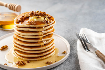 Tasty breakfast. Homemade pancakes with crushed walnut, honey or maple syrup on grey background.