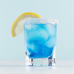 Refreshing alcohol drink blue Hawaii in misted rich shot glass with ice cubes, lemon slice, salt...