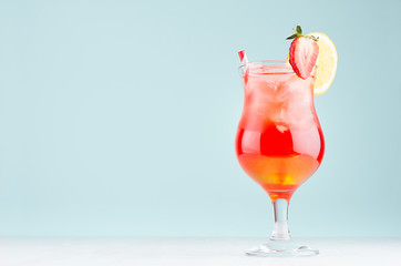 Fresh alcohol sunrise cocktail - red and yellow liquor, orange, ice, straw, strawberry in  wet...