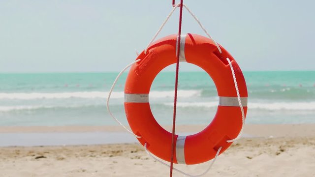 Red orange lifebuoy on a sandy beach in summer in the swimming season by the sea ocean, close-up