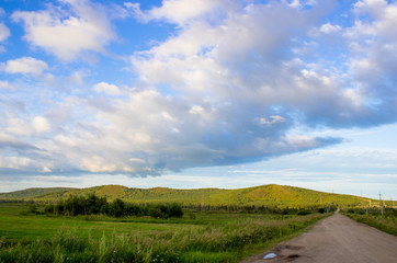Fototapeta premium Cloudy blue sky on the horizon of Russian fields and mountains. Summer forest on a sunny day.