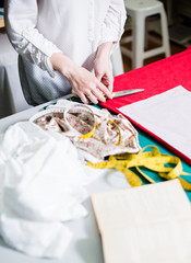 Hands of lady tailor working in her studio, tools and fabric samples on the sewing table