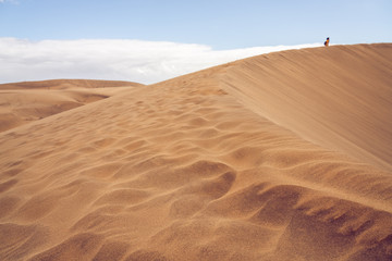 Scenic sand dune with people and sky in the background. Pretty dune formations in the foreground.