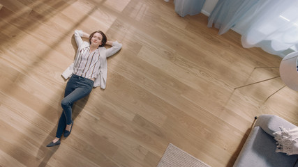 Young Woman is Lying on a Wooden Flooring in an Apartment. She's Dressed Casually. Cozy Living Room...