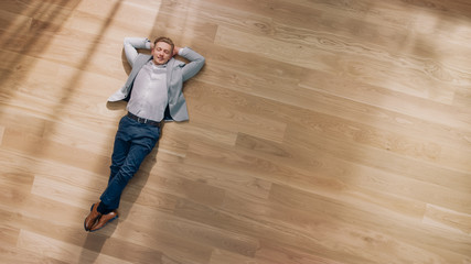 Young Man is Lying on a Wooden Flooring in an Apartment. He's Wearing a Jacket and White Shirt....