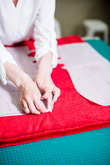 Hands of lady tailor working in her studio, tools and fabric samples on the sewing table