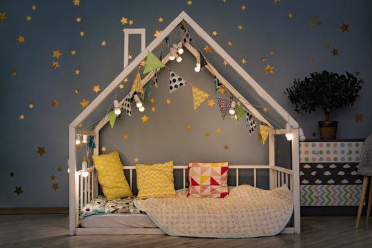 Modern kids bedroom in the evening. White house bed decorated with lights garland