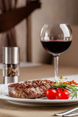 American cuisine. Beef steak with red bbq tomato sauce and cherry tomatoes. A glass of cool wine. Serving dishes on a white plate in a restaurant. Background image. copy space