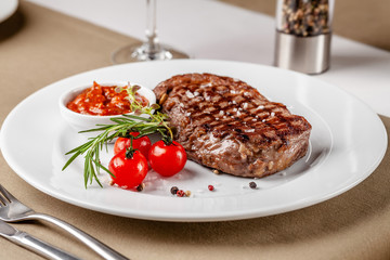 American cuisine. Beef steak with red bbq tomato sauce and cherry tomatoes. A glass of cool wine. Serving dishes on a white plate in a restaurant. Background image. copy space