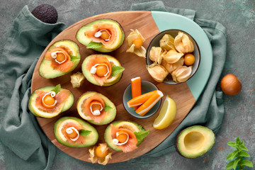 Avocado boats with smoked salmon, lemon, physalis and mint leaf, top view