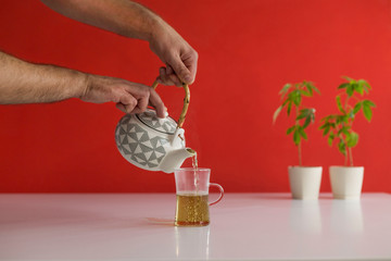 White table with Marijuana plant in pottery. Hand pouring hot CBD tea in to glass.