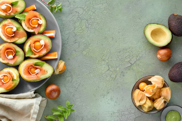 Avocado boats with smoked salmon, lemon, physalis and mint leaf, top view on green