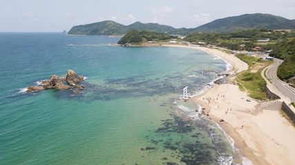 aerial footage of blue ocean, white wave and the twin rocks through the torii gate at the coast of sakurai futamigaura beach, itoshima fukuoka japan with tourists