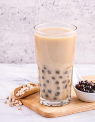 Popular Taiwan drink - Bubble milk tea with tapioca pearl ball in drinking glass on marble white table wooden tray background, close up, copy space