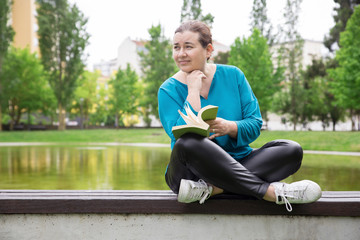 Pensive woman thinking over novel story. Thoughtful Caucasian lady sitting with legs crossed on...