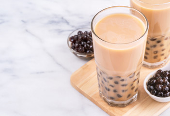 Popular Taiwan drink - Bubble milk tea with tapioca pearl ball in drinking glass on marble white table wooden tray background, close up, copy space
