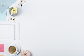 top view of cup of coffee, doughnut, book, pencils, glasses and binder clips on white