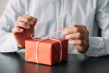 Corporate birthday party. Cropped shot of business man in shirt untying red gift box.