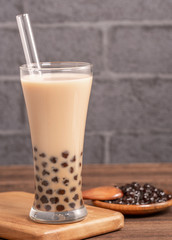 Popular Taiwan drink - Bubble milk tea with tapioca pearl ball in drinking glass and straw, wooden table gray brick background, close up, copy space