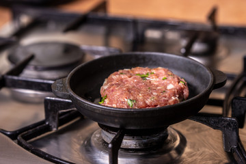 Iron pan with raw cutlet on a gas stove.