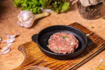 Iron frying pan with raw cutlet on a wooden board