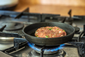 Iron pan with raw cutlet on a gas stove.