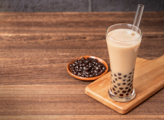 Popular Taiwan drink - Bubble milk tea with tapioca pearl ball in drinking glass and straw, wooden table gray brick background, close up, copy space