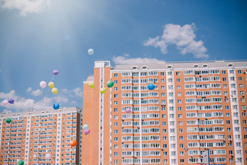 Multi-colored balloons against the blue sky, clouds and residential buildings. Last call and graduation at school