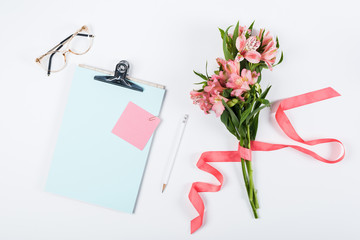 top view of flowers, clipboard, glasses, ribbon, paper and pencil on white
