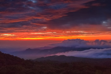 Obraz premium sunrise at Doi Inthanon, Km. 41 view point, mountain view misty morning on top hill with sea of mist in valley and red sun light in the sky background, Chiang Mai, Thailand.