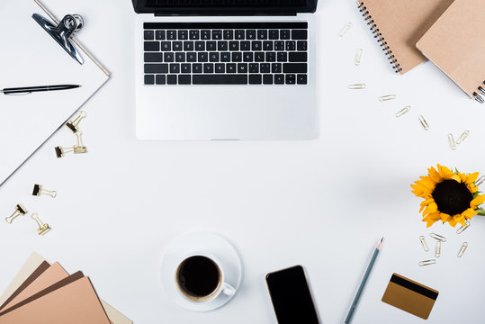 Top View Of Laptop, Smartphone With Blank Screen, Sunflower, Clipboard, Cup Of Coffee, Craft Paper, Credit Card, Binder Clips And Paper Clips On White