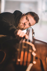Young luthier working in his workshop, building a double bass