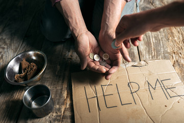 Fototapeta na wymiar Male beggar hands seeking money with sign HELP ME from human kindness on the wooden floor at public path way or street walkway. Homeless poor in the city. Problems with finance, place of residence.