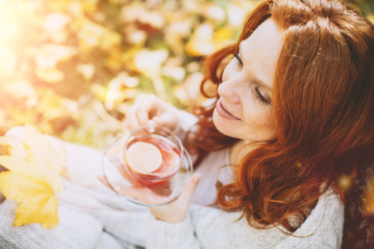 Portrait einer rothaarigen Frau im Herbst mit Bl&auml;ttern mit Teeglas trinkt Tee 